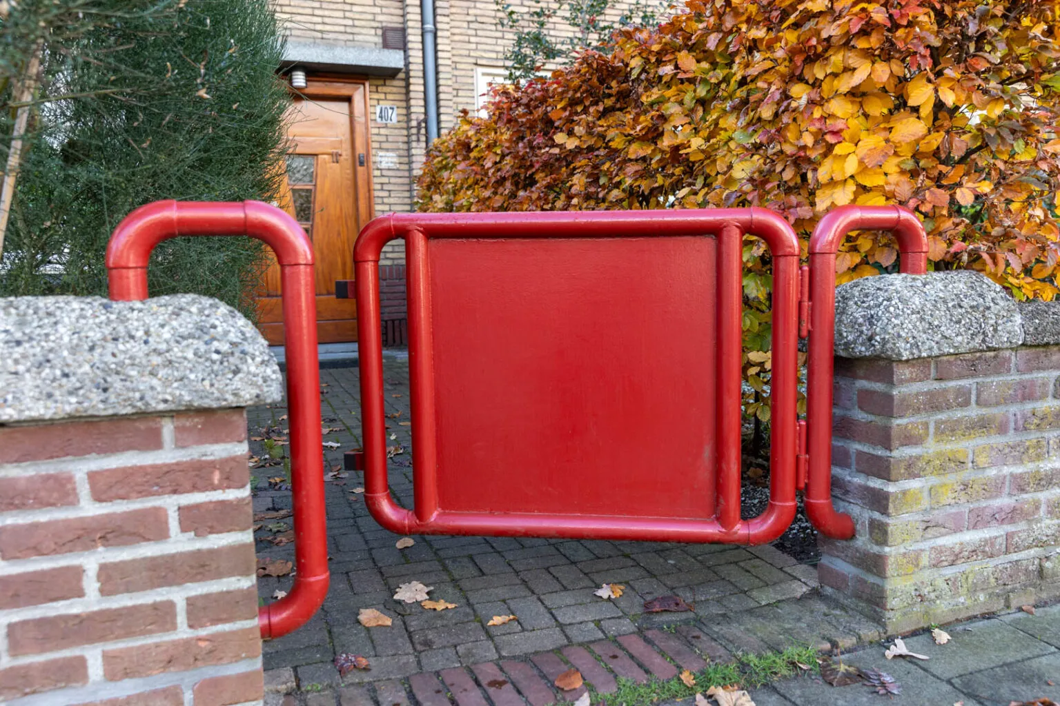 Gemetseld voortuinmuurtje met halfronde betonbanden van kiezel en rode poortbeugels