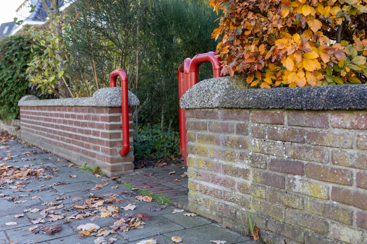 Rood geschilderde voortuinpoort tussen twee gemetselde muurtjes met betonbanden